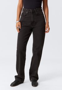 Hoge taille zwarte denim jeans met rechte pijpen, voorzien van vijf zakken en een knoopsluiting. De stof is stevig met een licht getextureerde afwerking.