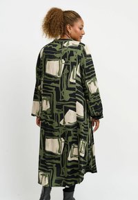 Rochie lungă neagră cu un model abstract verde și bej, mâneci lungi, croi lejer și o siluetă fluidă. Material moale care se așază delicat.