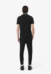 T-shirt en coton noir avec un logo sur le col, associé à un pantalon de jogging noir. Présente une coupe slim et un design sobre, complété par des baskets noires.