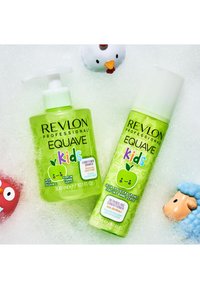 Groene shampoo- en conditionerflessen met speelse appelgrafieken, een gladde textuur en een pompdispenser. Bellen en kleine speelgoedjes op de achtergrond.