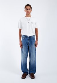White cotton t-shirt with short sleeves, blue denim wide-leg jeans, and brown shoes, standing on a plain light background.