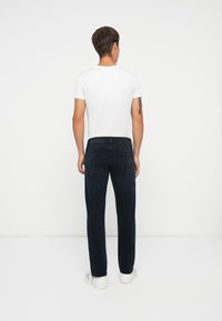 Jeans de mezclilla oscura con un corte recto, detalles mínimos, diseño de cinco bolsillos y una cinturilla negra sólida, combinados con una camiseta blanca.