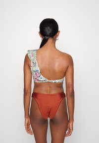 Top de bikini assimétrico com padrão floral, borda franzida e parte de baixo bronze de cintura alta com detalhes gathered. Textura suave.
