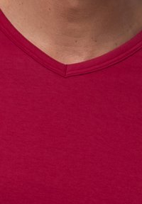 Rød bomulds T-shirt med V-hals, der har en glat tekstur, korte ærmer og en forstærket søm ved halsen. Diskret meleret mønster synligt.