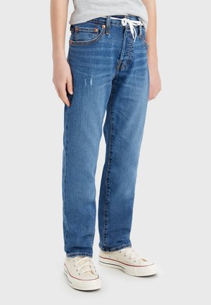 Jean en denim bleu coupe droite, avec un cordon blanc, des rivets en cuivre et des zones subtilement décolorées sur le tissu.