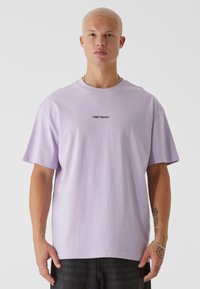Lilla oversized t-skjorte laget av bomull med rund hals. Har teksten "LOST YOUTH" i svart sentrert på brystet.