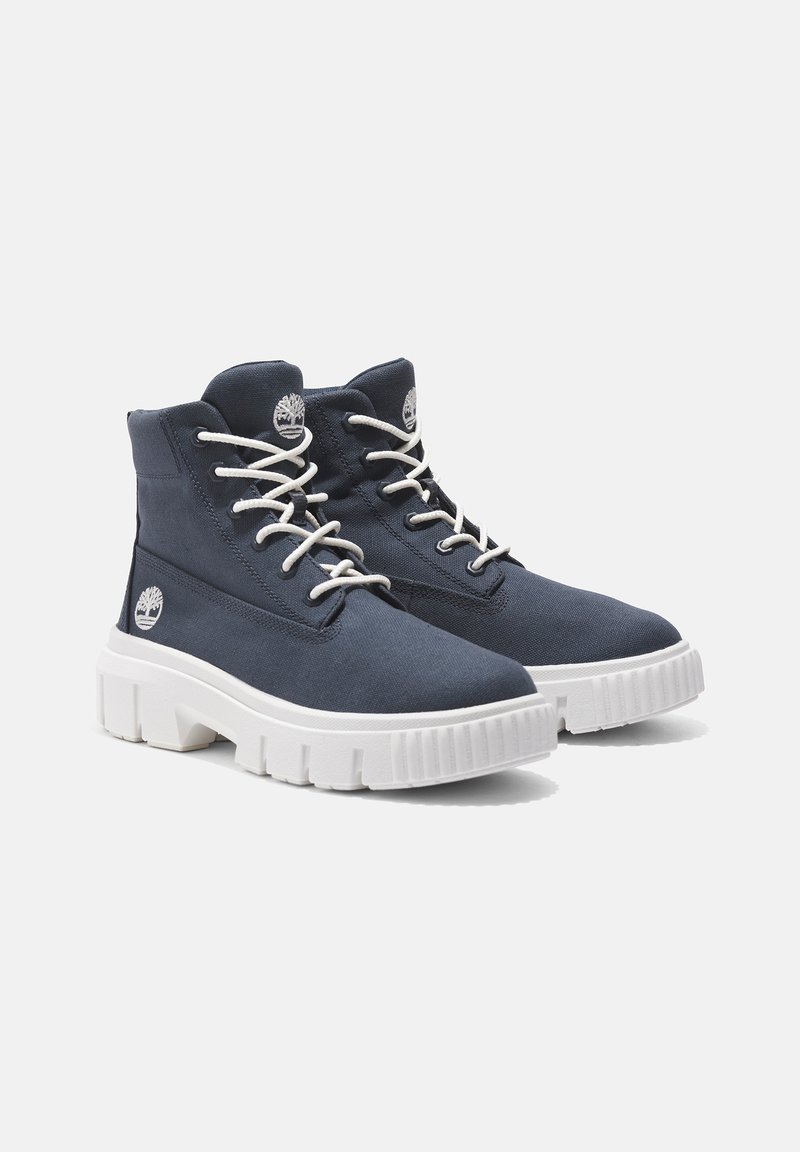 Marineblaue hohe Stiefel aus Stoff, mit weißen Schnürsenkeln, einer weißen dicken Sohle und einem kleinen Logo an der Seite.