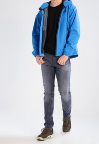 Blå vattentålig jacka med huva, grå foder, elastiska ärmslut. Tillsammans med en svart tröja, grå jeans och bruna sneakers med gröna accenter.