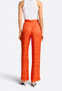 Orangene, blumenmusterte, hochgeschnittene Hose mit geradem Bein, aus glattem Stoff, kombiniert mit schimmernden Absatzsandalen.