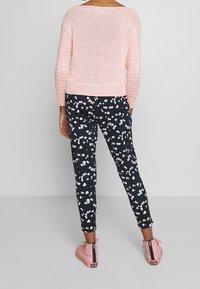 Ljusrosa stickad tröja med trekvartsärmar, kombinerad med marinblå blommiga byxor och rosa hög-top sneakers.