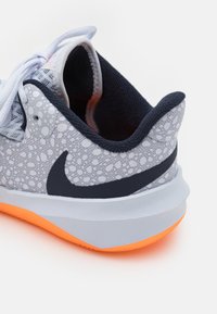 Scarpa da ginnastica grigia con tomaia testurizzata a pois, dettagli blu navy e suola arancione. Presenta un collare imbottito e design con lacci.