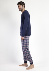 Camisa de manga larga navy con cuello redondo, combinada con pantalones de pijama de cuadros rojos y azules con puños elásticos y un ajuste cómodo.