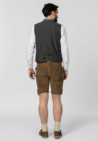 Braune Leder-Shorts kombiniert mit einer grauen strukturierten Weste. Die Weste hat einen Verschluss hinten. Darunter ein weißes Hemd.