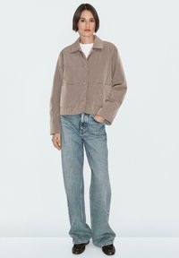 Geknipte, beige jas met een kraag, twee frontrijzakken en ronde knopen, gecombineerd met lichtblauwe wijde jeans en zwarte schoenen.