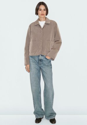Geknipte, beige jas met een kraag, twee frontrijzakken en ronde knopen, gecombineerd met lichtblauwe wijde jeans en zwarte schoenen.