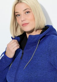 Felpa blu con tessuto testurizzato, chiusura con zip e foderatura nera. Presenta cordini e un colletto alto. Slim fit sulle spalle.
