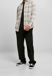 Langarm geruite blouse in wit, zwart en rood, met een relaxte pasvorm, gecombineerd met zwarte corduroybroeken en zwarte sneakers.