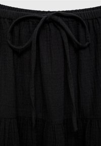 Jupe noire à volants en tissu texturé. Dotée d'une ceinture élastique avec un cordon noué et de détails froncés à l'ourlet.