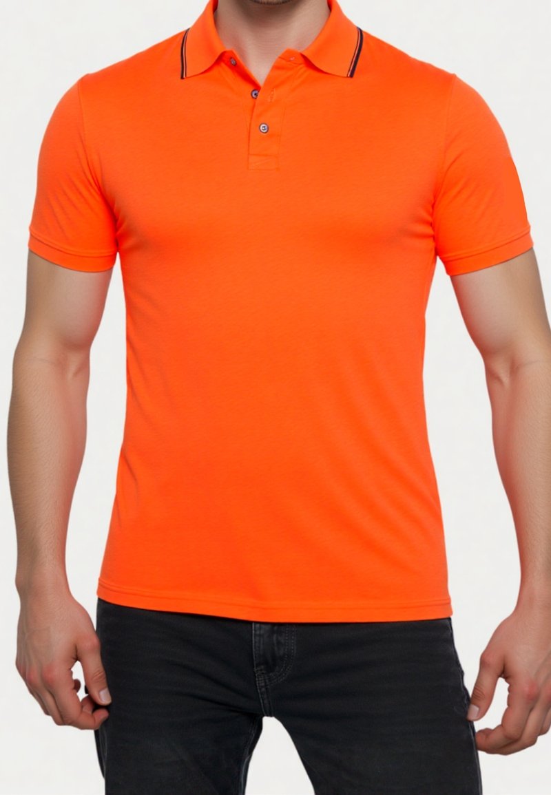 Homme portant un polo ajusté à manches courtes de couleur orange vif avec un col bordé de noir et un jean foncé, debout devant un fond blanc.
