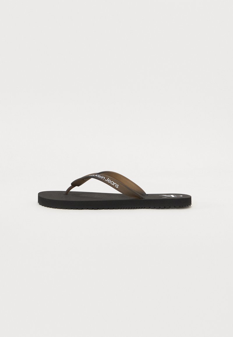 Barna gumiflip-flop, textúrált fekete talppal, sima pánttal és fehér logóval. Lapos dizájn és laza stílus.