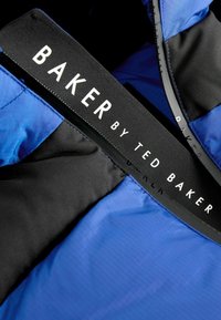 Unutrašnjost plave i crne jakne s glatkom teksturom, s istaknutom crnom etiketom na kojoj piše "BAKER by TED BAKER."