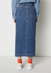 Denim maxiskjol i medelblått med rak skärning, bakfickor och rå kant. Matcher med vita sneakers och orangea strumpor.