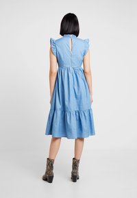 Světle modré deninové šaty s vrstevnatou sukní, volánkovými rukávy a detailem klíčové dírky na zádech. Kombinované s vzorovanými kotníkovými botami.