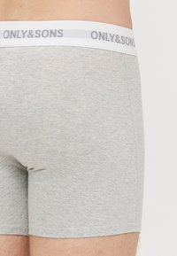 Harmaat puuvillaiset bokserishortsit, joissa on tiukka istuvuus ja valkoinen joustava vyötärönauha, johon on painettu harmaalla tekstillä "ONLY&SONS".