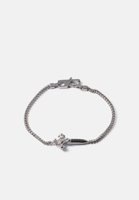 Pulseira de metal prateado com um design de corrente trançada, com um acento central de cruz adornado com pedras claras e pretas.