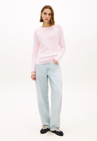 Ανοιχτό ροζ πλεκτό πουλόβερ με στρογγυλή λαιμόκοψη, συνδυασμένο με ανοιχτό μπλε τζιν παντελόνι φαρδιάς γραμμής και μπλε σκούρα μπαλαρίνες. Απλό, καθημερινό σύνολο.