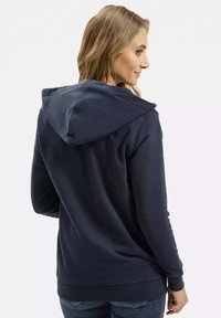 Granatowa bluza z kapturem wykonana z miękkiego materiału, z kieszenią kangurką i ściągaczami przy rękawach, o luźnym kroju, pokazana z tyłu.