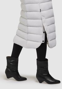 Hvid pufferjakke med ribbet tekstur og knaplukning. Sorte læderankelstøvler med spids tå og kilehæl, båret over sorte leggings.