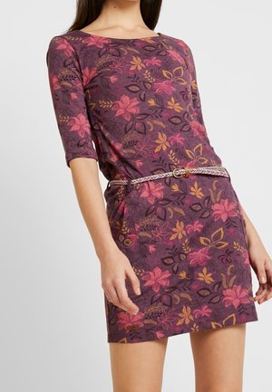 Frau trägt ein lila Blumenmusterkleid mit pinken und gelben Blumen, dreiviertel Ärmeln und einem geflochtenen beigen Gürtel in der Taille.