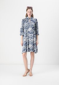 Abito blu e bianco a fantasia con colletto, maniche corte e corpetto arricciato. Silhouette leggermente svasata. Completato da sandali nude con tacco alto.
