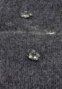 Tessuto grigio a maglia con trama visibile, caratterizzato da accenti metallici decorativi e gemme multicolori incorporate nella tessitura.