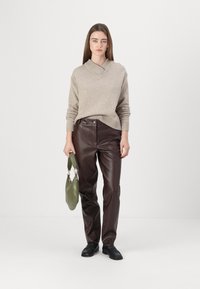 Pulover bej tricotat cu guler în V, pantaloni din piele ecologică maro cu o finisare texturată, geantă verde și pantofi negri.