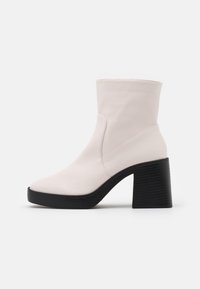 White leather ankle boot with rounded toe and chunky black block heel on plain white background, side view.