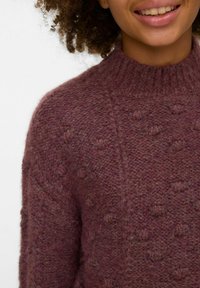 Dziļi mauves krāsas džemperis ar teksturētu bumbu rakstu un ribotas apļveida apkakles izgriezumu, izceļot mīkstu, biezas dzijas siltumu.