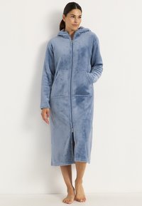 Fleece zip-up morgonrock i ljusblått, med huva, långa ärmar, två sidofickor och hel dragkedja. Mjuk textur, längd till mitten av vaddern.