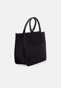 Borsa tote nera con texture in pizzo, accentuata da un tessuto liscio, forma strutturata, due manici e una ampia apertura sulla parte superiore.