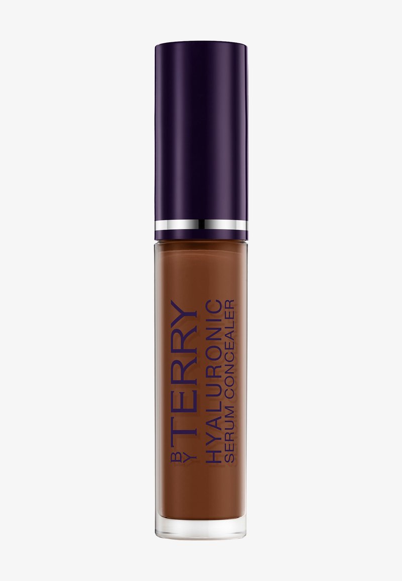 Concealer-flaske med mørkebrun væske, gennemsigtig beholder og mørkelilla låg med etiketten "By Terry Hyaluronic Serum Concealer."