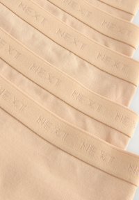 Colanți bej cu o textură netedă, având un elastic marcat cu "NEXT" într-un design subtil, reliefat. Așezați într-un rând.