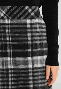 Jupe en tartan noir et blanc en tissu de laine texturé, présentant des épaisseurs de bandes variables et des motifs à carreaux distincts au niveau de la taille et de l'ourlet.