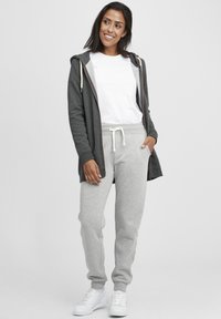 Grå zip-up hoodie över en vit t-shirt, tillsammans med ljusgrå mjukisbyxor och vita sneakers. Tyget verkar mjukt och avslappnat.