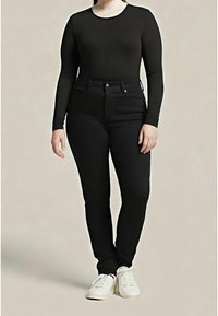 Černý top s dlouhým rukávem a černé úzké džíny. Oblečení má přiléhavý střih a hladkou texturu, doplněné o bílé tenisky.