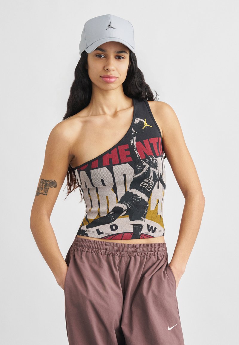 Débardeur gris asymétrique avec des graphismes audacieux représentant un joueur de basketball ; tissu doux et coupe décontractée associée à un pantalon marron ample.