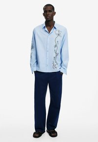 Light blue cotton shirt with floral embroidery on the left side, paired with navy pants and black sandals. Long sleeves and button closure.