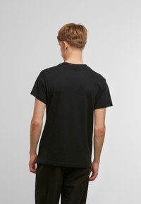Sort T-shirt med korte ærmer lavet af bomuld, med rund hals og afslappet pasform, vist fra ryggen mod en lys grå baggrund.