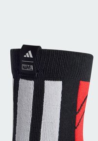 Calcetín negro hasta la rodilla con rayas verticales blancas y un diseño gráfico rojo. Incluye una etiqueta negra bordada con "ADIDAS" y "MARVEL".