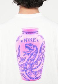 Valge T-särk, millel on suur roosa vaasi graafika, sinise madude ja lillemotiividega ning sõna "NIKE" rasvases kirjas.